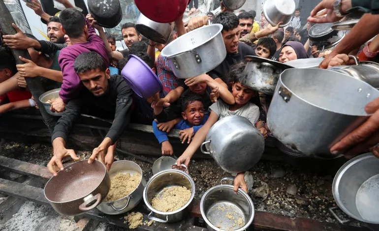 Palestinians wait to receive food cooked by a charity kitchen, in Jabalia, in the northern Gaza Strip, on May 14, 2025